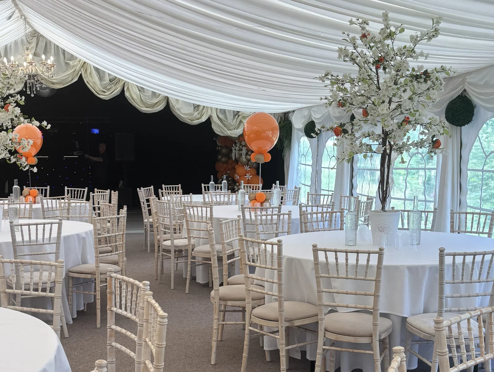 Luxury marquee interior at Downham Hall decorated with orange balloons and white blossom trees for a private party.