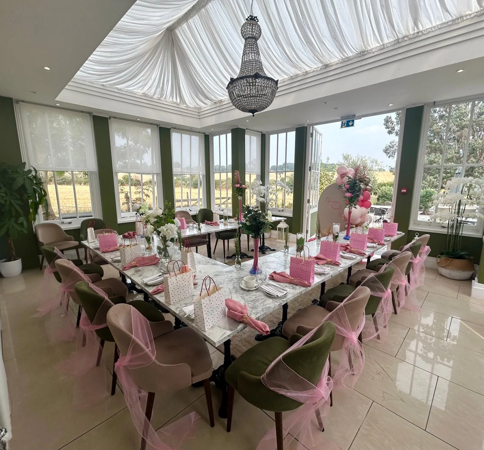 A decorated private party table with pink gift bags and floral arrangements in The Orangery at Downham Hall.