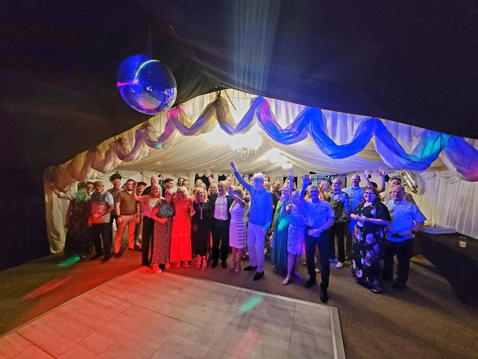 A large group of guests enjoying an evening party with a disco ball and dance floor in the Downham Hall marquee.