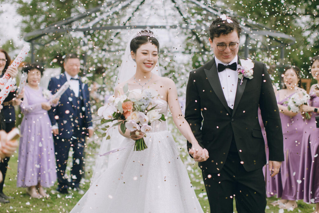 Bride and groom walking under floral arch during confetti exit at Downham Hall wedding venue in Essex