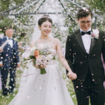 Bride and groom walking under floral arch during confetti exit at Downham Hall wedding venue in Essex