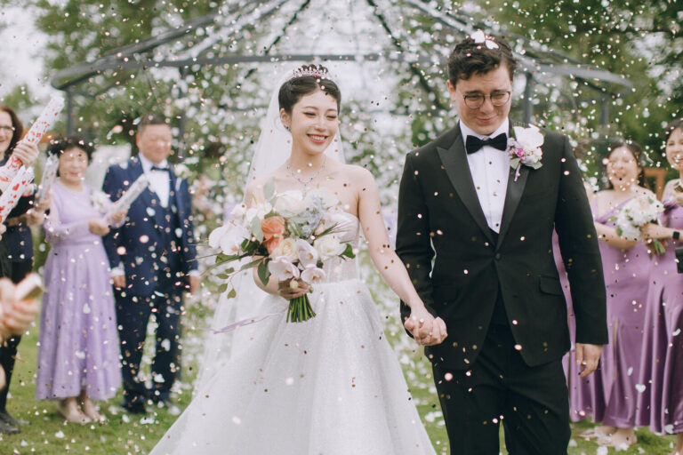 Bride and groom walking under floral arch during confetti exit at Downham Hall wedding venue in Essex