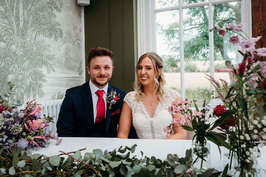 Bride and groom seated at decorated reception table at Downham Hall wedding venue in Essex