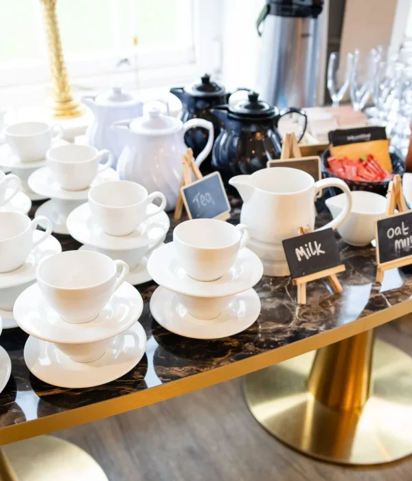 A professional coffee and tea refreshment station with white china cups and milk carafes on a marble table at Downham Hall.