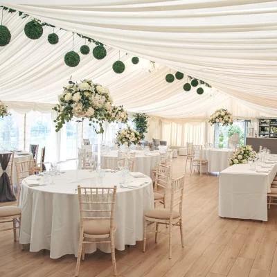 Luxury Marquee Interior at Downham Hall Spacious luxury marquee with white draped ceilings, floral centerpieces, and round tables for large events in Essex.