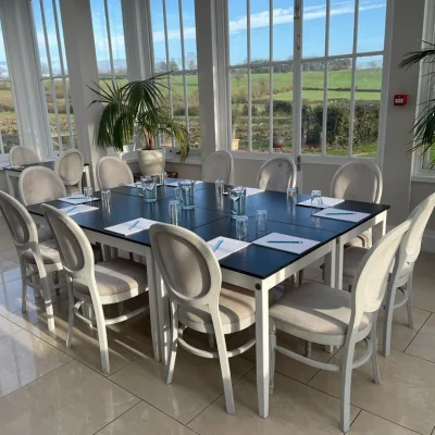 A circular meeting table with white chairs and notebooks under a chandelier in the light-filled Downham Hall Orangery.
