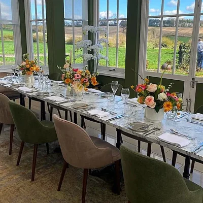 Private Dining Table in the Orangery A long marble dining table with floral centerpieces and views of the Essex countryside through large windows in the Orangery.